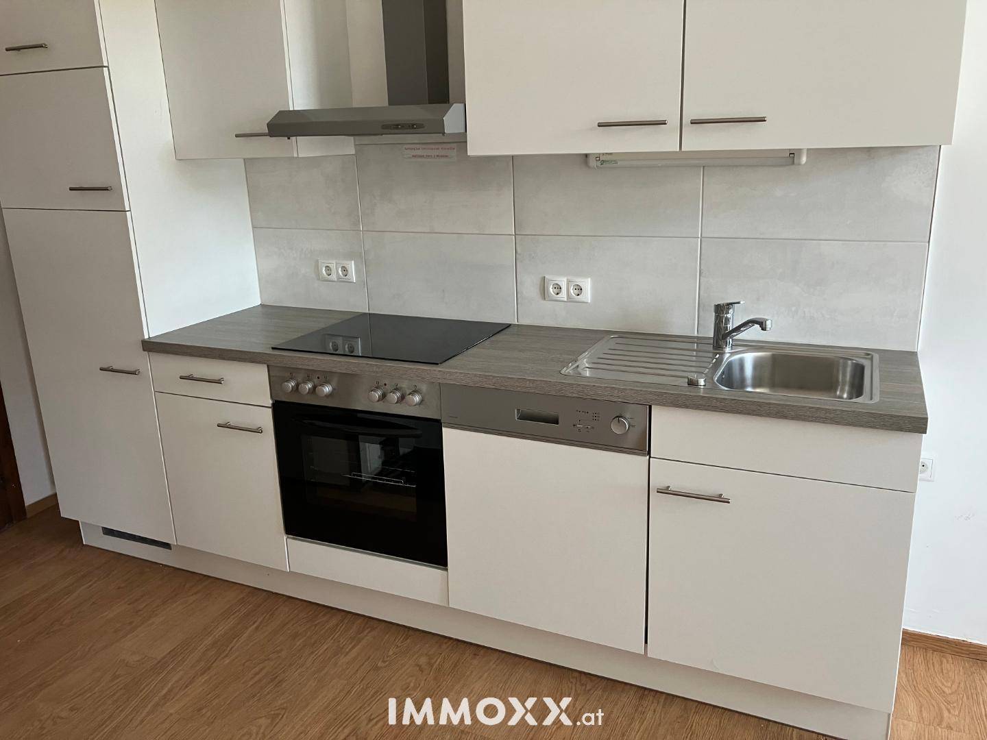 Moderne Einbauküche mit Induktionskochfeld, Backofen, Geschirrspüler und weißen Schränken.