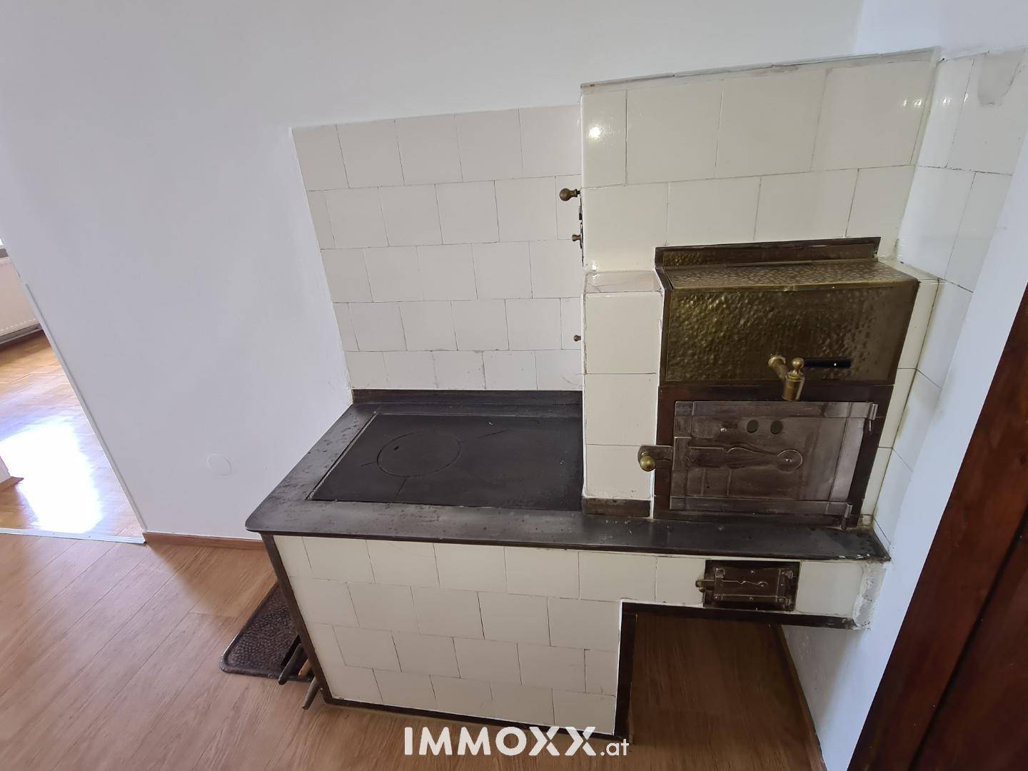 Detailansicht eines traditionellen Kachelofens mit Kochfläche und verzierter Metalltür.