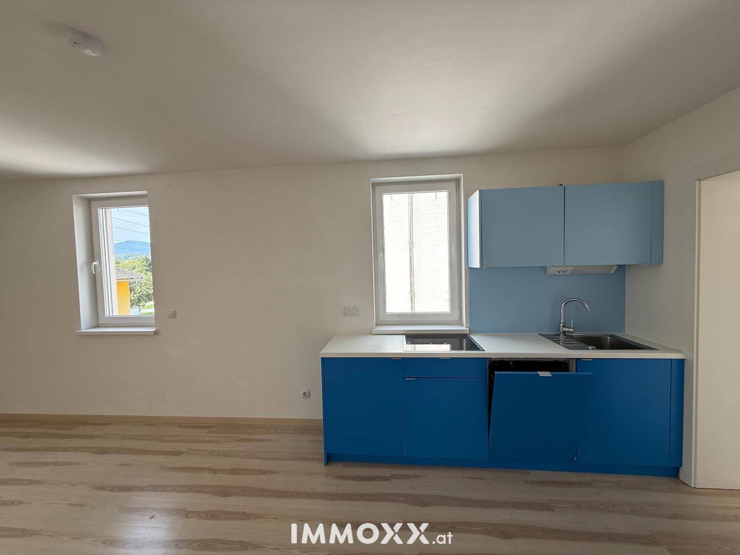 Helle Küchenzeile in Blau mit Spüle, Kochfeld und Fenstern für Tageslicht.