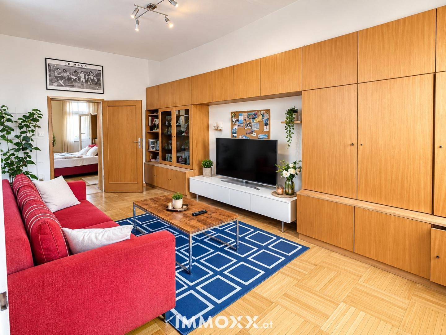 Gemütliches Wohnzimmer mit Holzeinbauschränken, rotem Sofa und Blick ins Schlafzimmer.