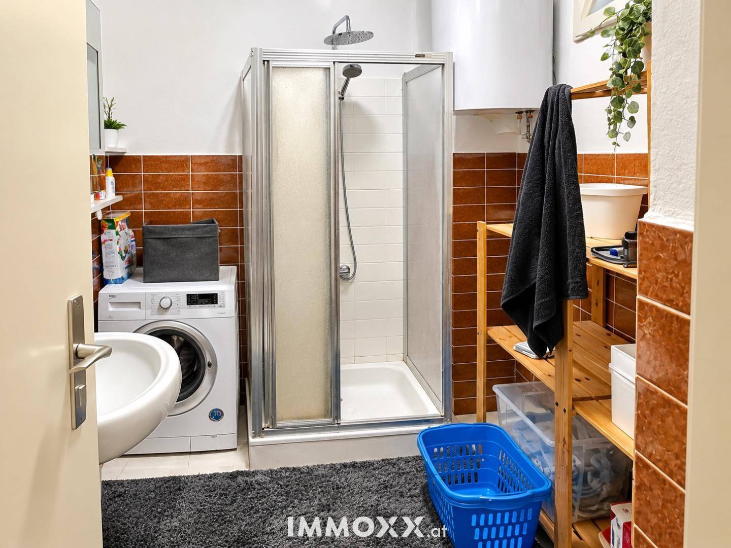 Funktionales Badezimmer mit Duschkabine, Waschmaschine und braunen Wandfliesen.