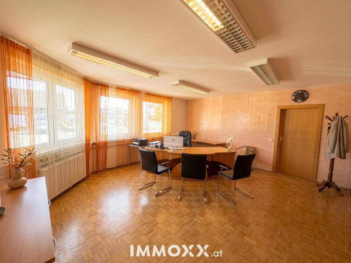 Helles Büro mit Holzparkettboden, großen Fenstern mit orangefarbenen Vorhängen und moderner Büroeinrichtung.