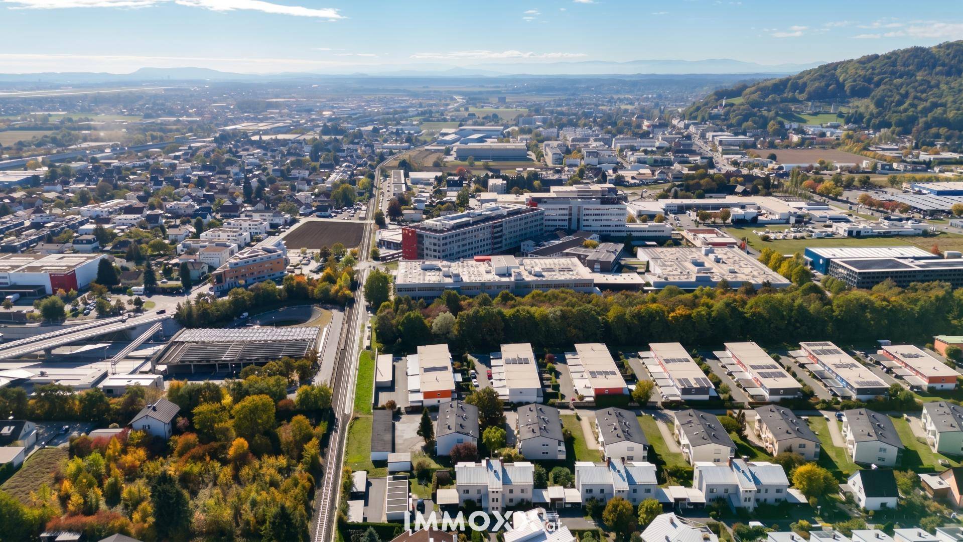 Luftaufnahme einer Stadt mit Wohngebieten, Gewerbeflächen und angrenzender Naturlandschaft.