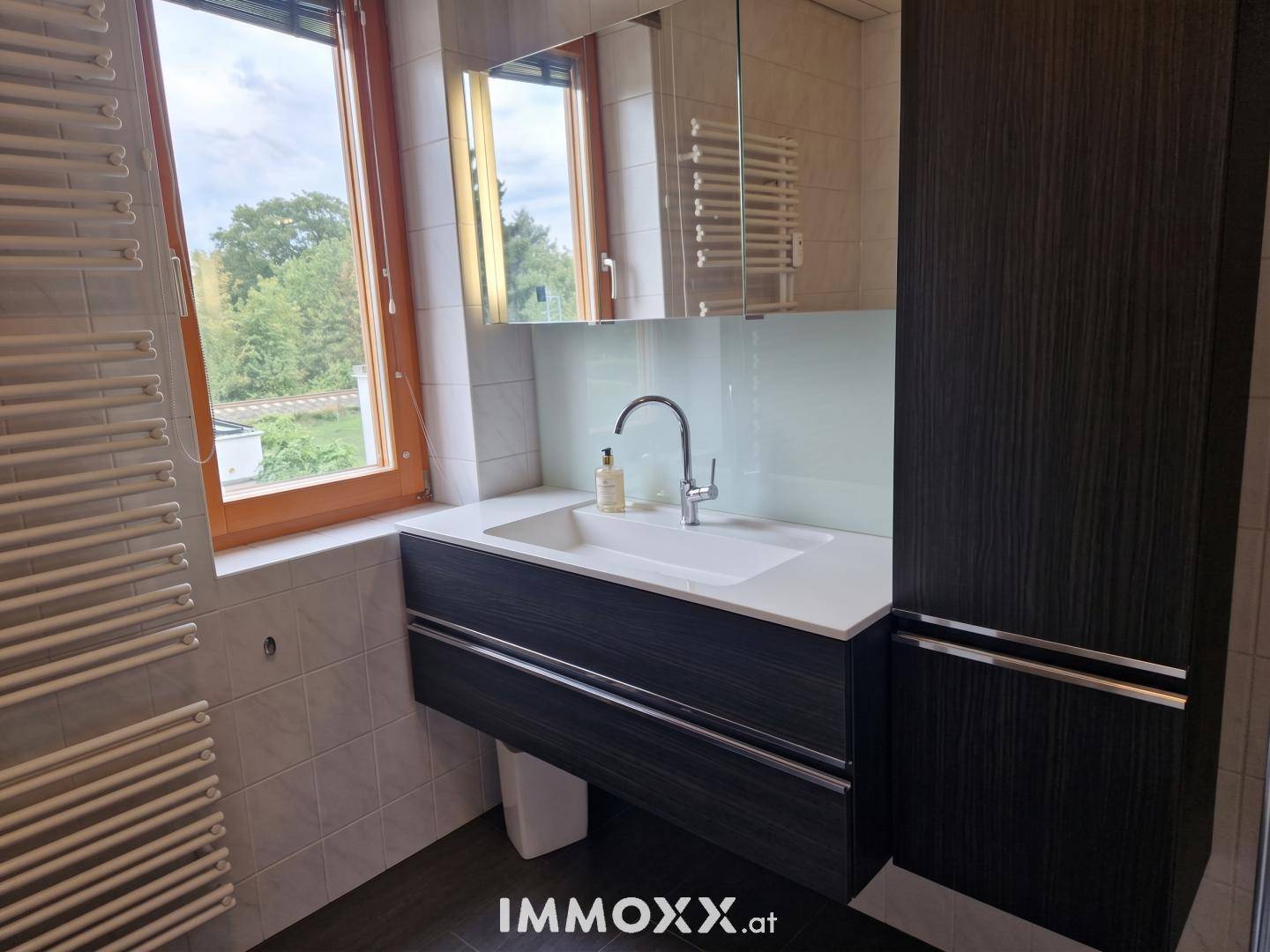 Waschtischbereich im Badezimmer mit modernem Unterschrank, Spiegelschrank und Fenster.