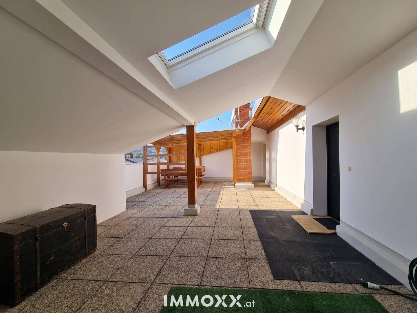 Helle Dachterrasse mit großem Oberlicht, Fliesenboden und Holzpergola, bietet viel Platz im Freien.