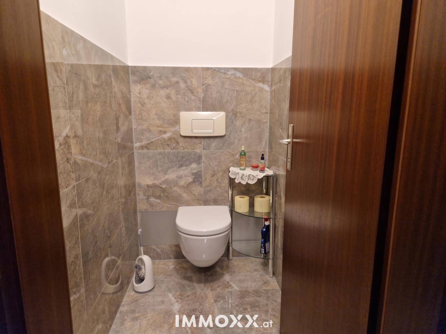 Separates WC mit wandhängender Toilette und modernen Fliesen an den Wänden.
