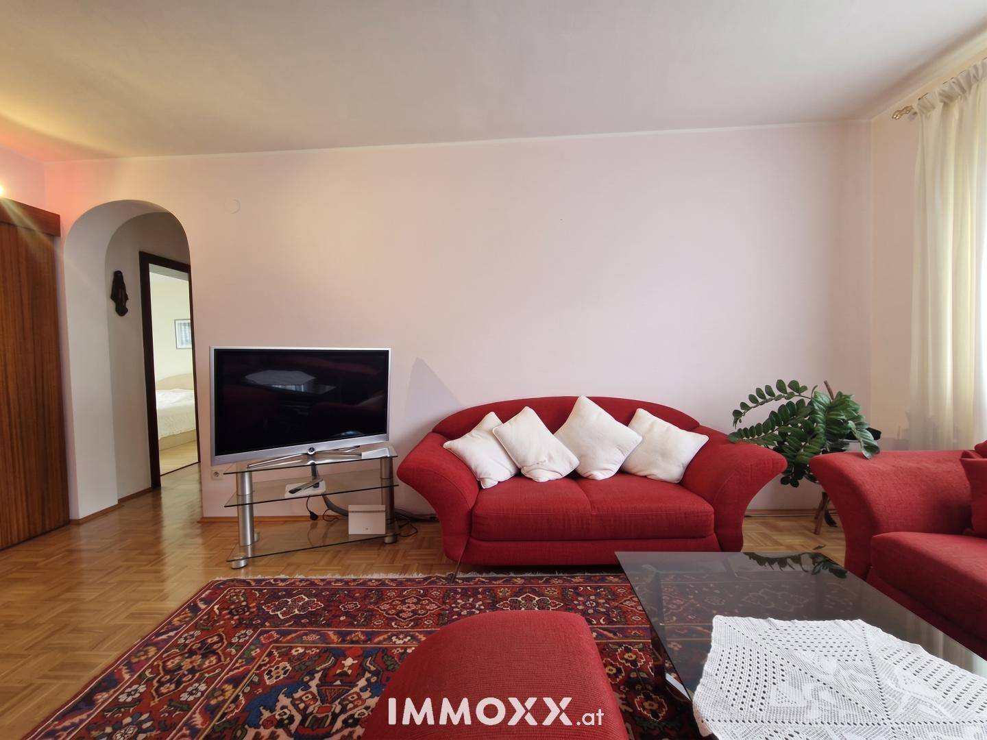 Wohnzimmer mit bequemen roten Sofas, Fernseher und einem traditionellen Teppich, lädt zum Entspannen ein.
