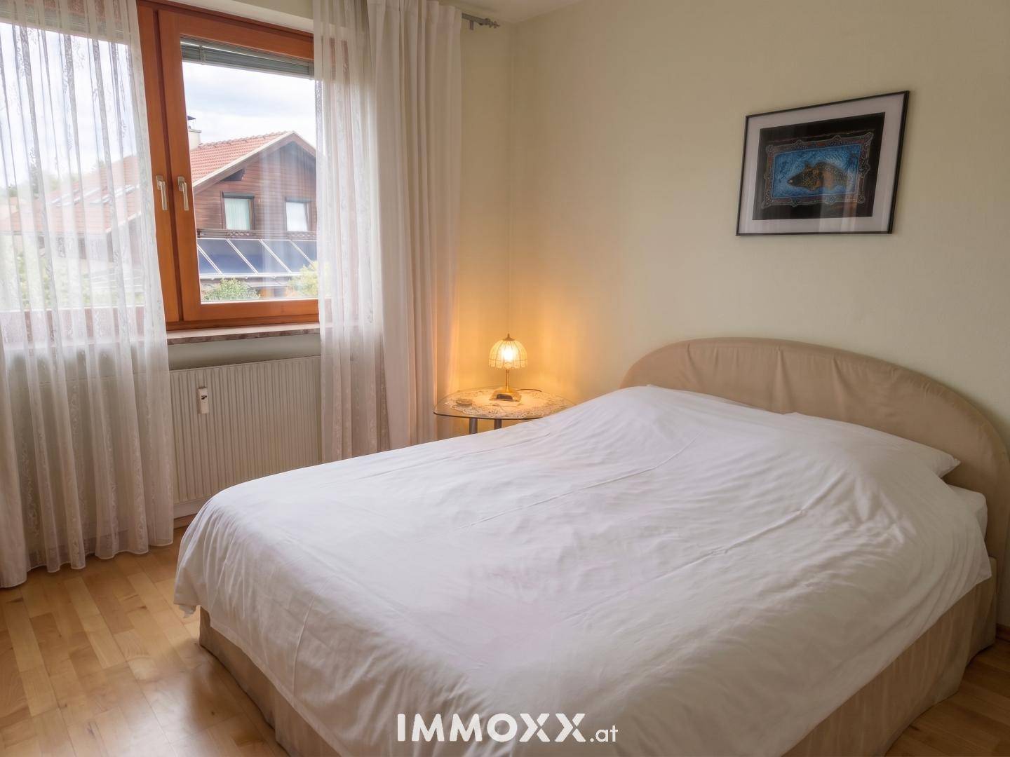 Schlafzimmer mit Doppelbett und einfacher Einrichtung, durch das Fenster fällt viel Tageslicht.