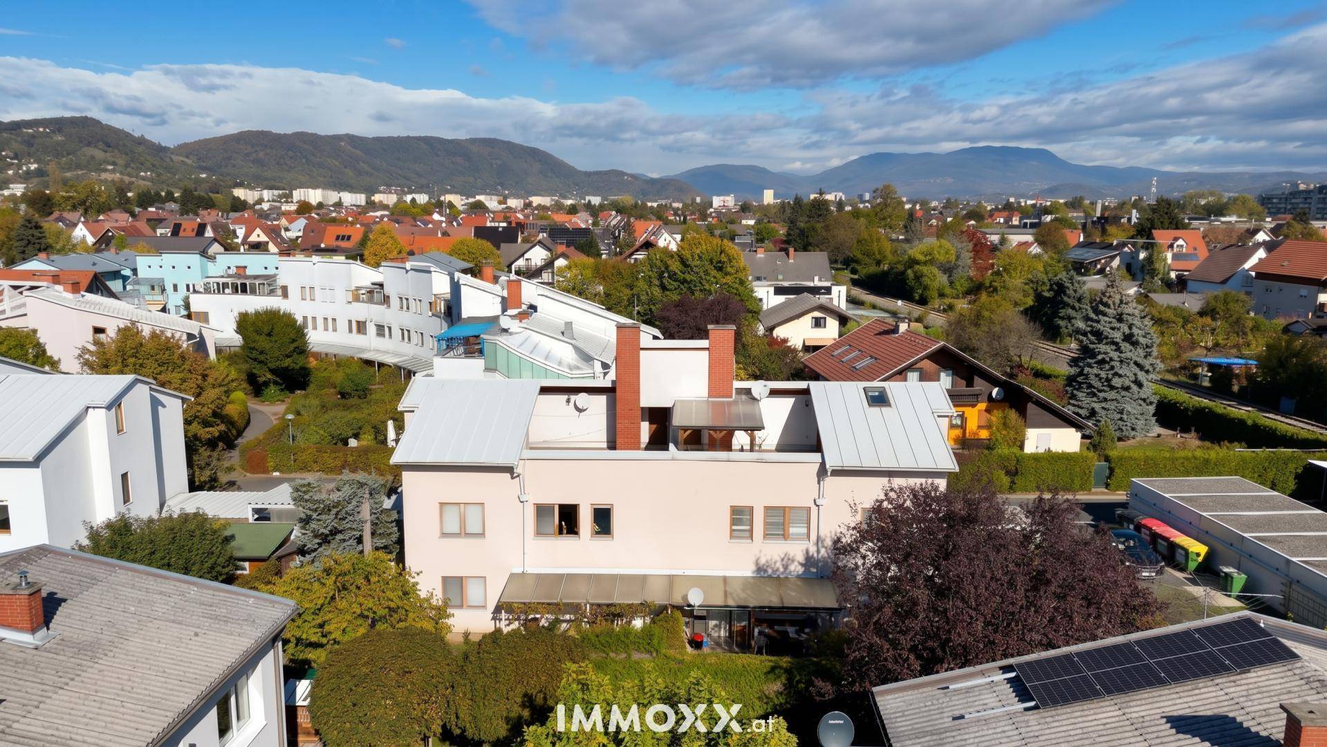Luftaufnahme eines Wohnhauses mit Garten und umliegenden Gebäuden, umgeben von grünen Hügeln.