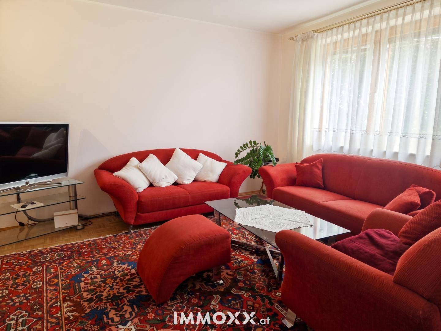 Helles Wohnzimmer mit roten Sofas, Couchtisch und großen Fenstern, die viel Licht hereinlassen.