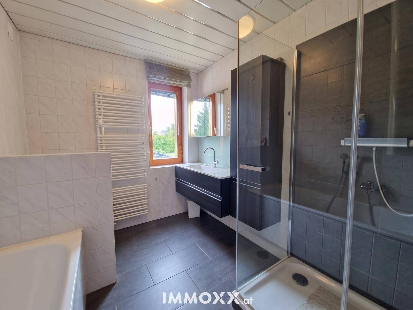 Modernes Badezimmer mit Dusche, Badewanne, Waschtisch und beheiztem Handtuchhalter.
