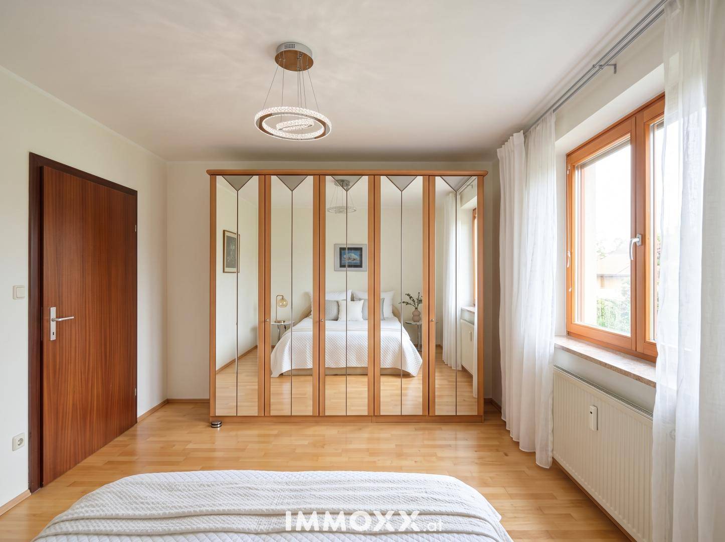 Geräumiges Schlafzimmer mit großem Spiegelschrank und hellem Parkettboden, wirkt sehr einladend.