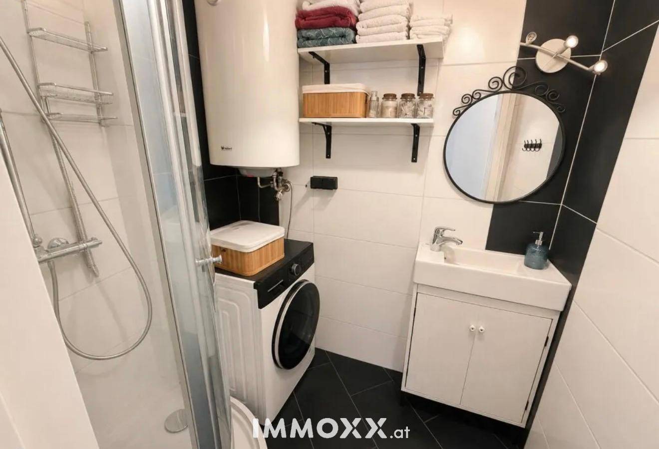 Modernes Badezimmer in Schwarz-Weiß mit Dusche, Waschmaschine und Waschbecken.
