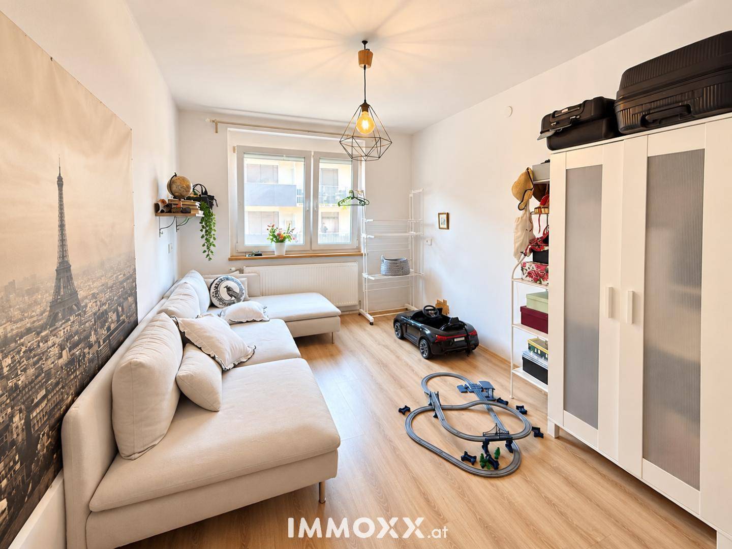 Helles Zimmer mit Sofa, Laminatboden und großem Fenster, ideal als Kinder- oder Gästezimmer.