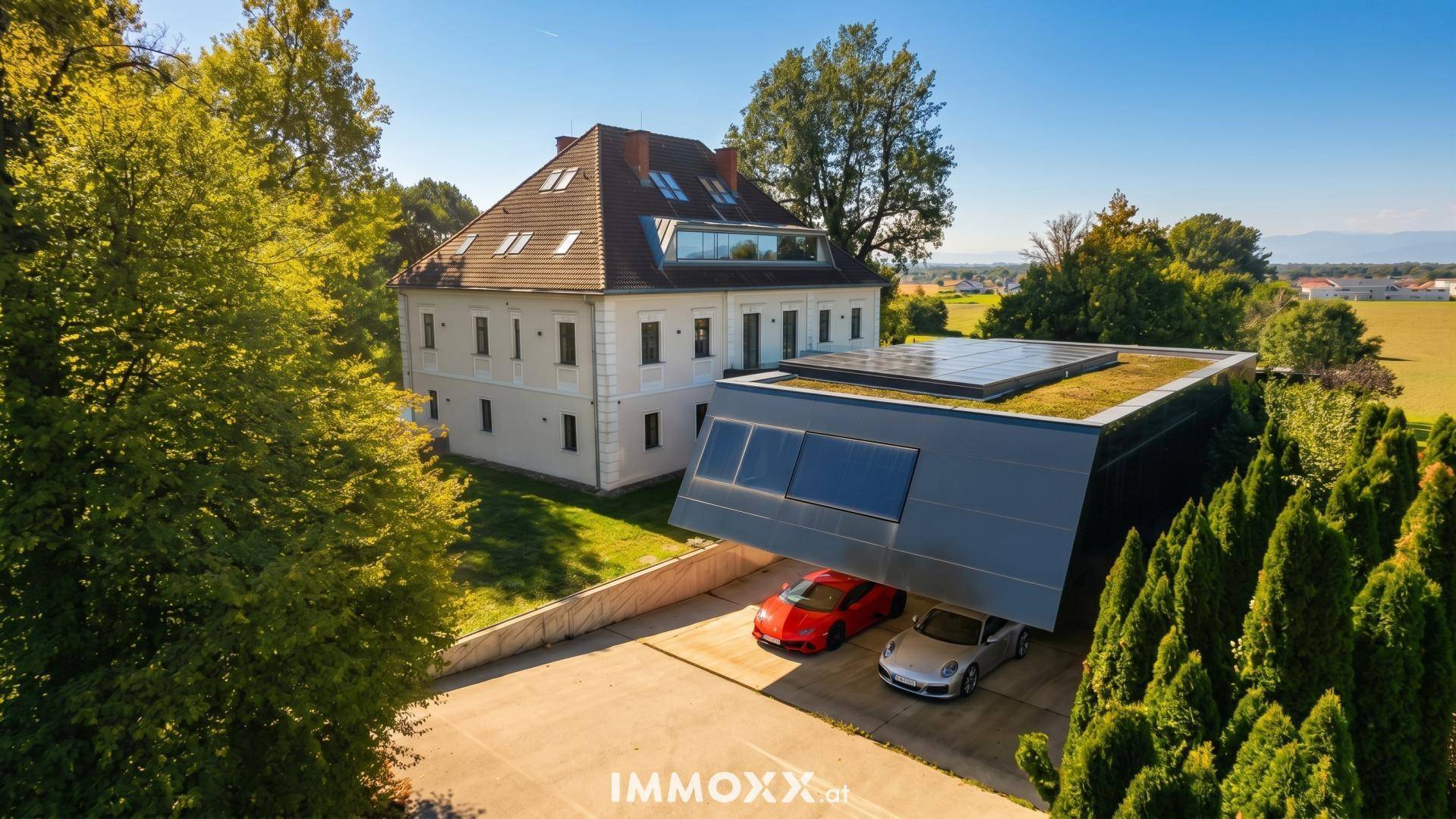 Anwesen mit historischem Hauptgebäude, modernem Anbau und Carport für Fahrzeuge.
