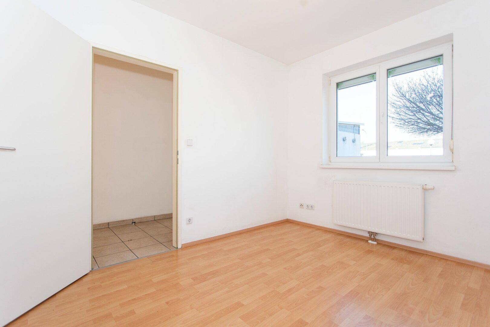 Helles Schlafzimmer mit Fenster, Heizkörper und Laminatboden, bietet einen Blick ins Freie.