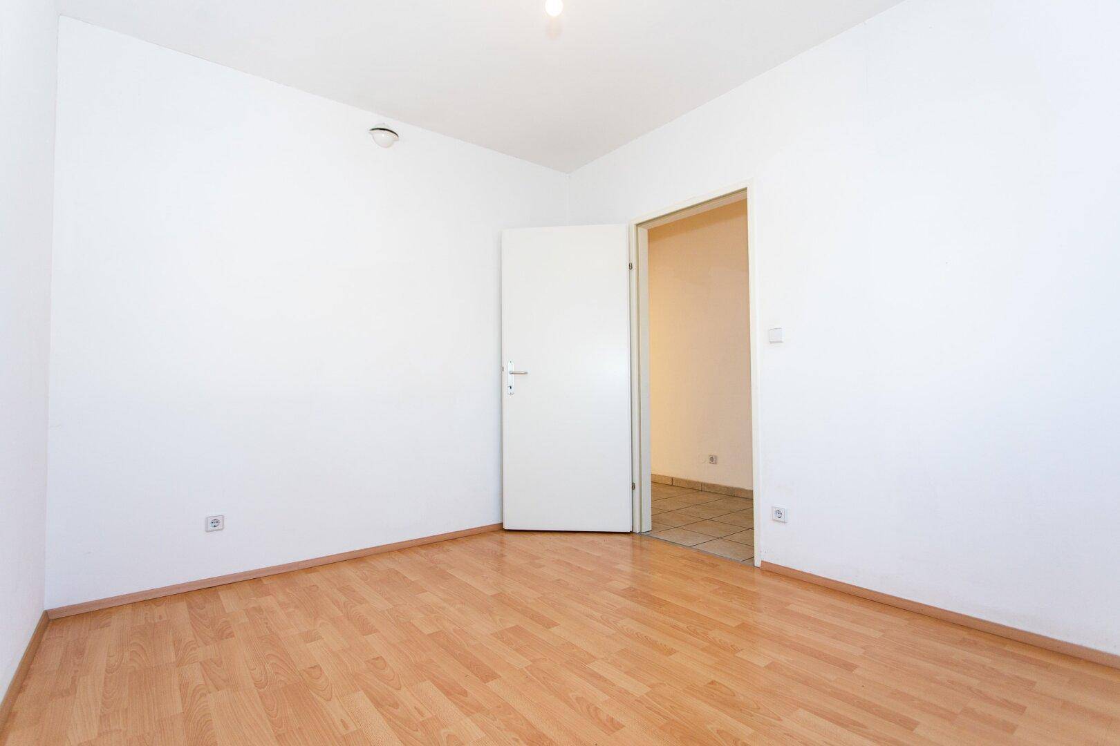 Leeres Schlafzimmer mit Laminatboden und weiß gestrichenen Wänden, bereit zur individuellen Gestaltung.