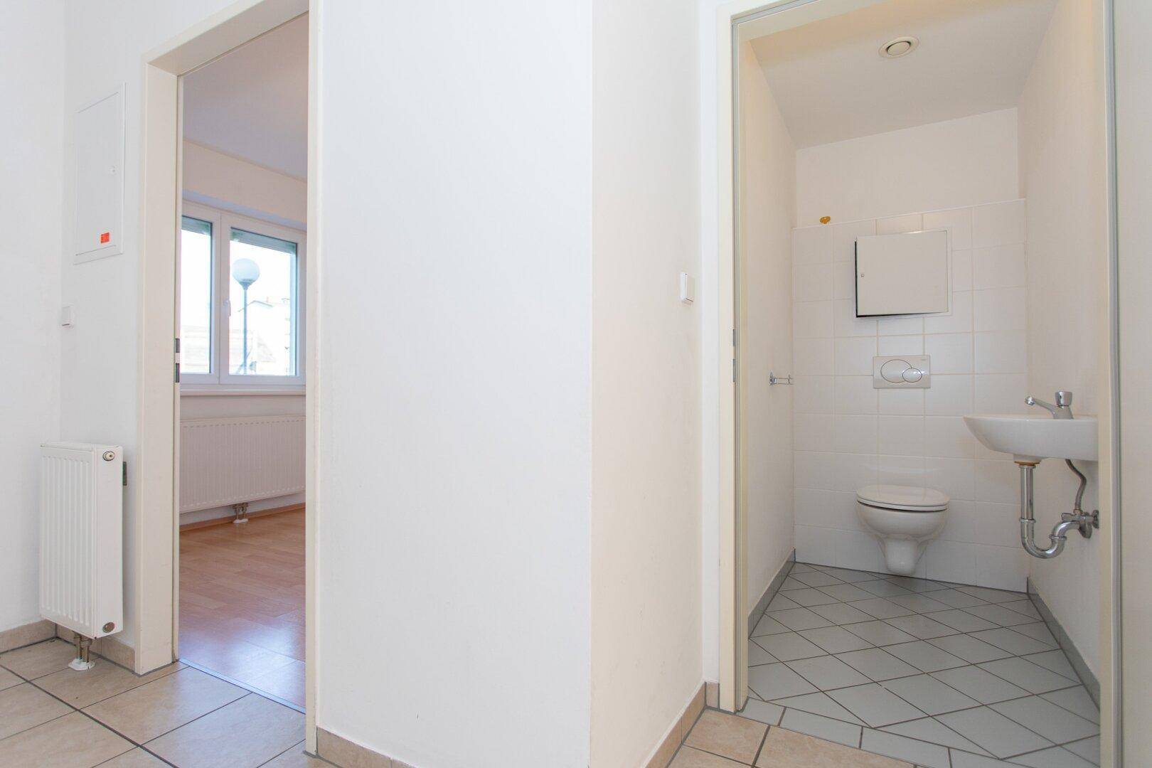 Heller Flur mit Fliesenboden, der zu einem kleinen Gäste-WC und weiteren Räumen führt.