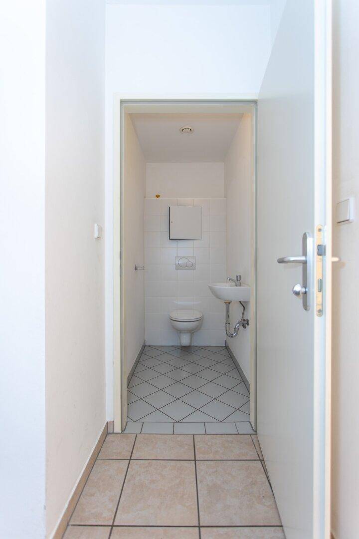 Kleines Gäste-WC mit weiß gefliesten Wänden und grauem Fliesenboden, funktional und sauber.