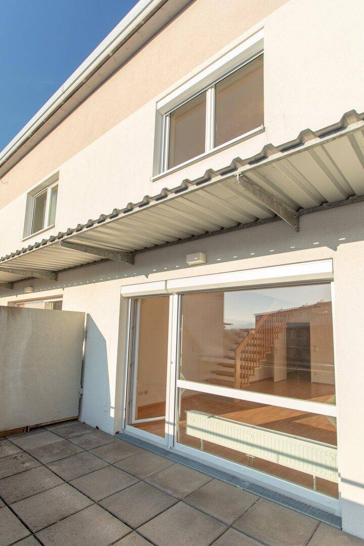 Helle Terrasse mit Fliesenboden und Einblick in den Wohnbereich mit Treppe, bietet viel Tageslicht.