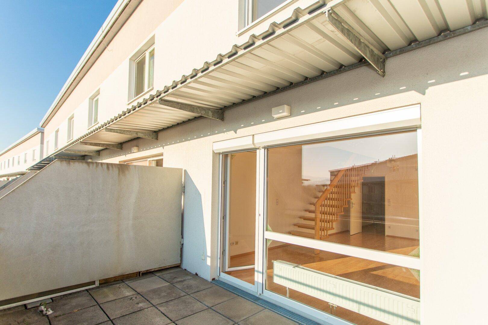 Geräumige Terrasse mit Blick in das helle Wohnzimmer und die Holztreppe, ideal für sonnige Tage.