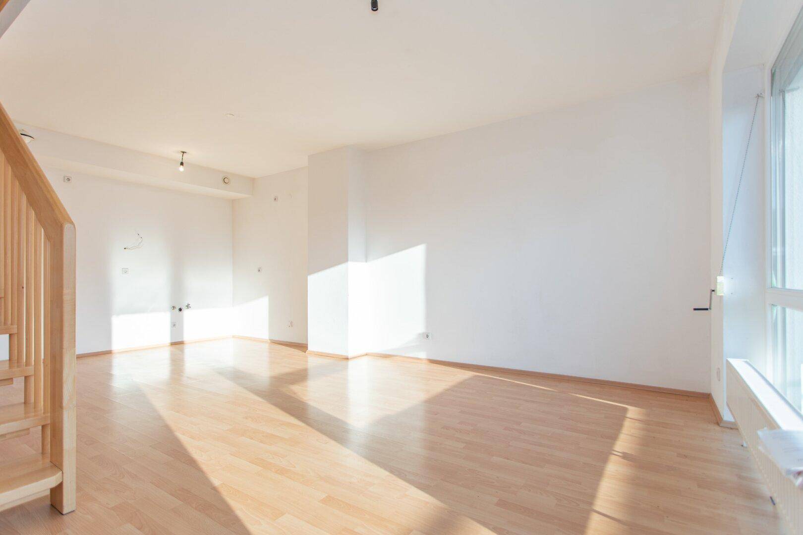 Geräumiges Wohnzimmer mit viel Tageslicht und Laminatboden, bietet eine helle und offene Atmosphäre.