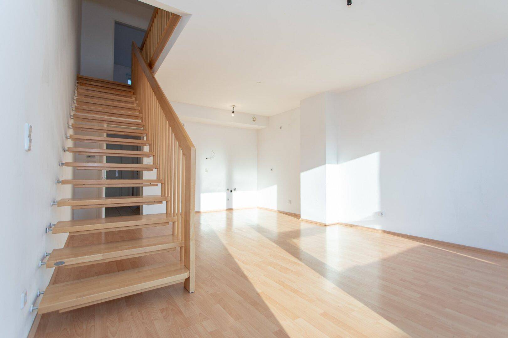 Offener Wohnbereich mit heller Holztreppe und Laminatboden, durchflutet von natürlichem Licht.