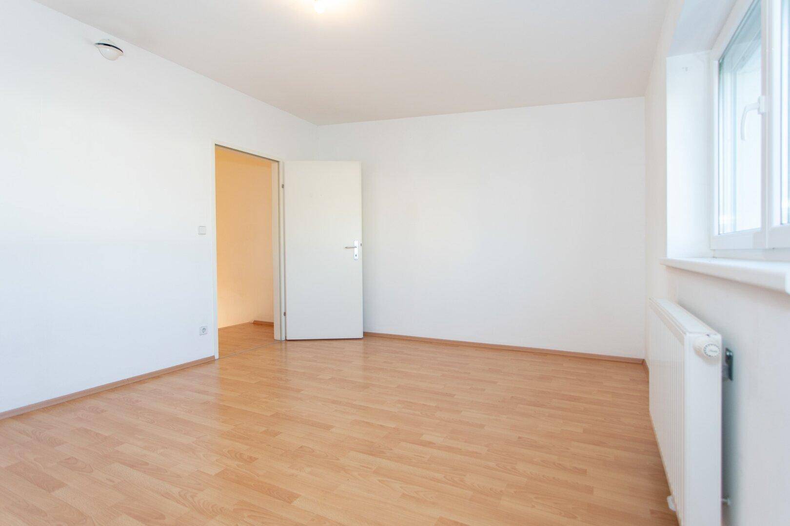 Helles Schlafzimmer mit Laminatboden und Fenster, bereit für die individuelle Gestaltung.