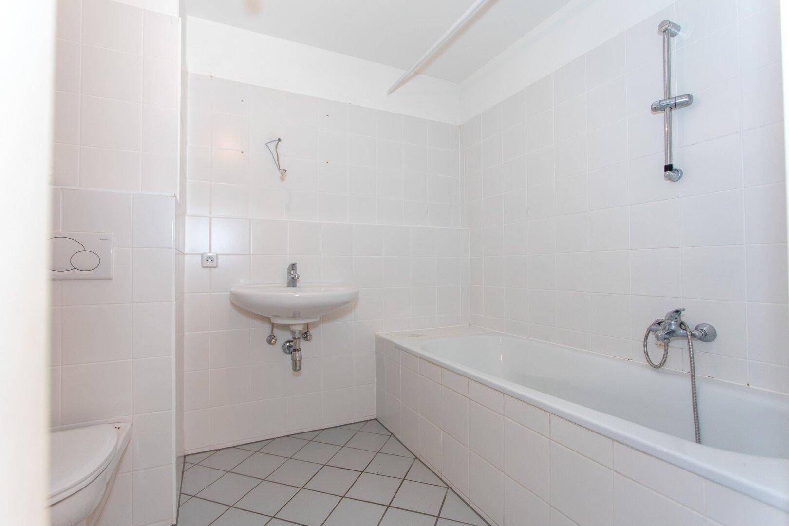 Funktionales Badezimmer mit Badewanne, Waschbecken und WC, komplett weiß gefliest.