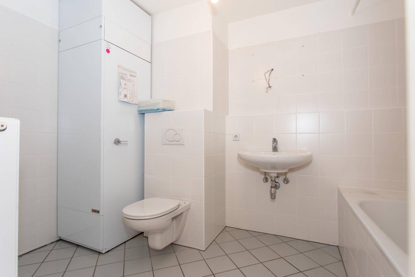 Helles Badezimmer mit Badewanne, Waschbecken und WC, ausgestattet mit weißen Fliesen und Heizkörper.