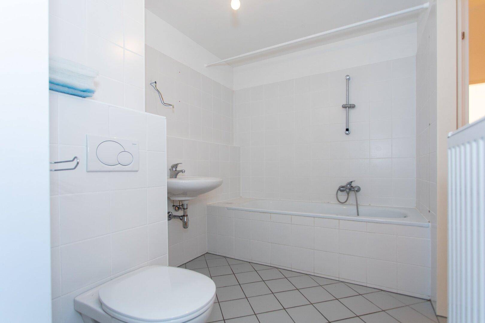 Modernes Badezimmer mit Badewanne, Waschbecken und WC, komplett in Weiß gehalten und gefliest.