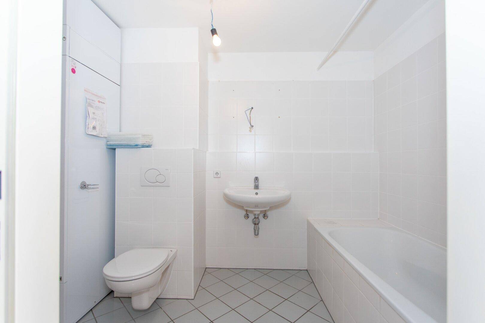 Funktionales Badezimmer mit Badewanne, Waschbecken und WC, in hellen Farben gehalten und gefliest.