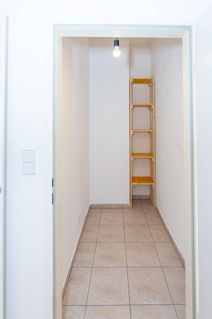 Kleiner, heller Abstellraum mit Fliesenboden und einem einfachen Holzregal für zusätzlichen Stauraum.