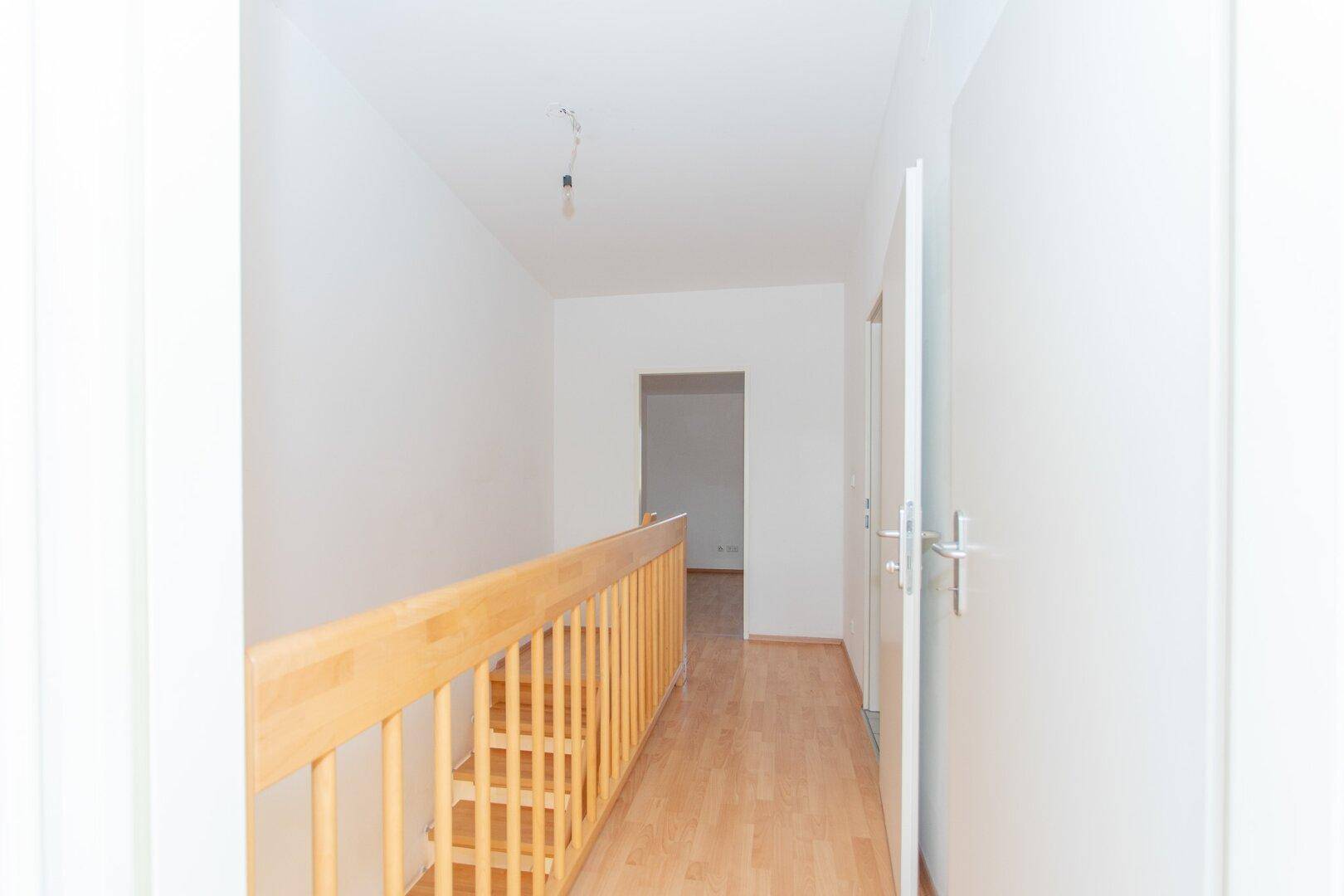 Heller Flur mit Laminatboden und einem Holztreppengeländer, das zu weiteren Räumen führt.