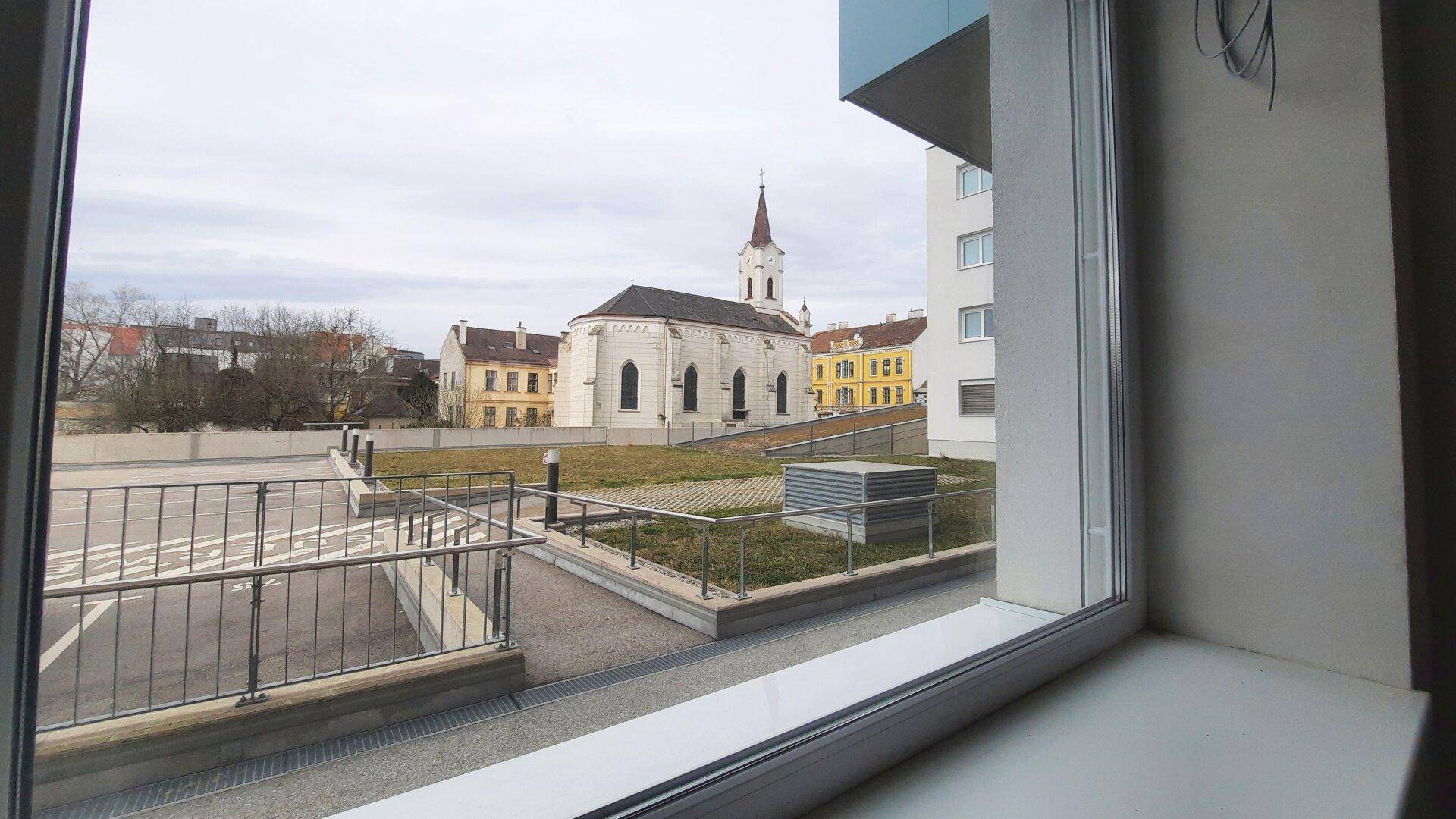 Blick aus dem Fenster auf eine Kirche, umliegende Gebäude und einen Außenbereich mit Parkplätzen.