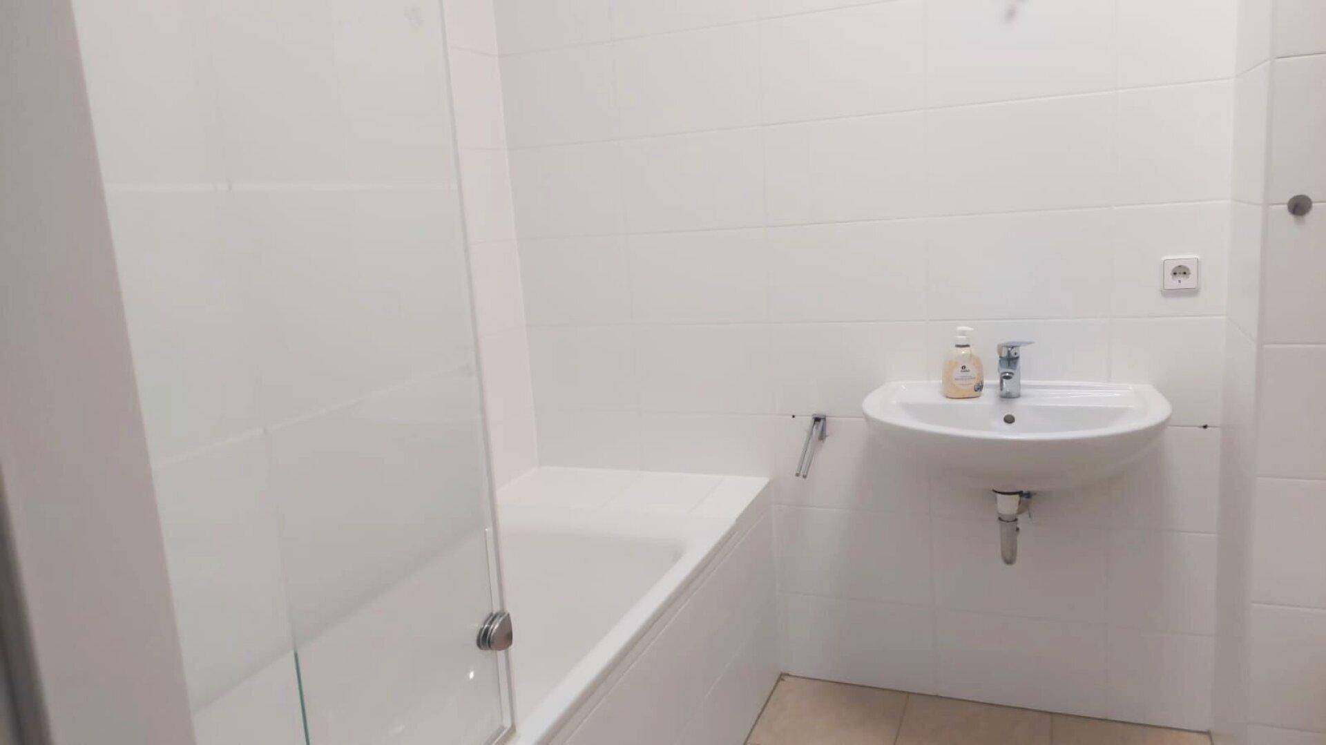 Helles Badezimmer mit Badewanne inklusive Duschabtrennung und modernem Waschbecken.