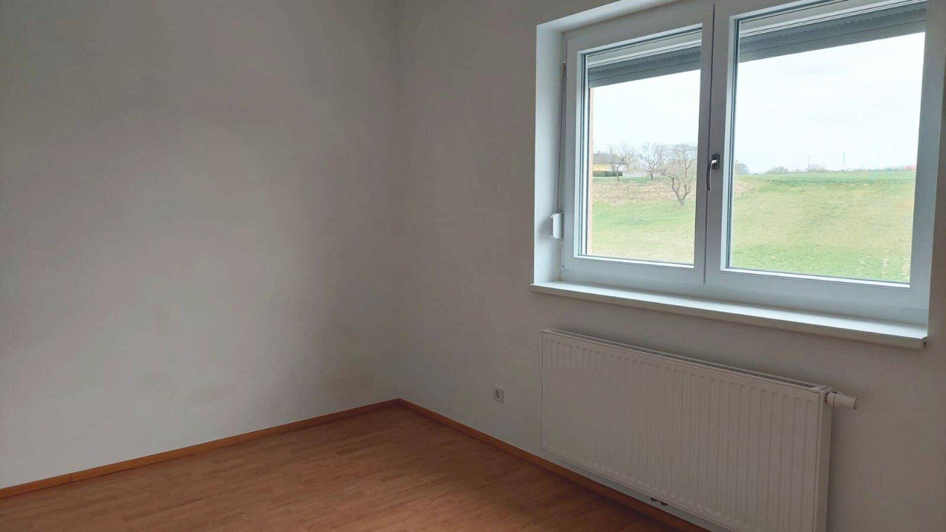 Freundliches Schlafzimmer mit Laminatboden und Fenster, das einen direkten Blick auf eine grüne Wiese bietet.