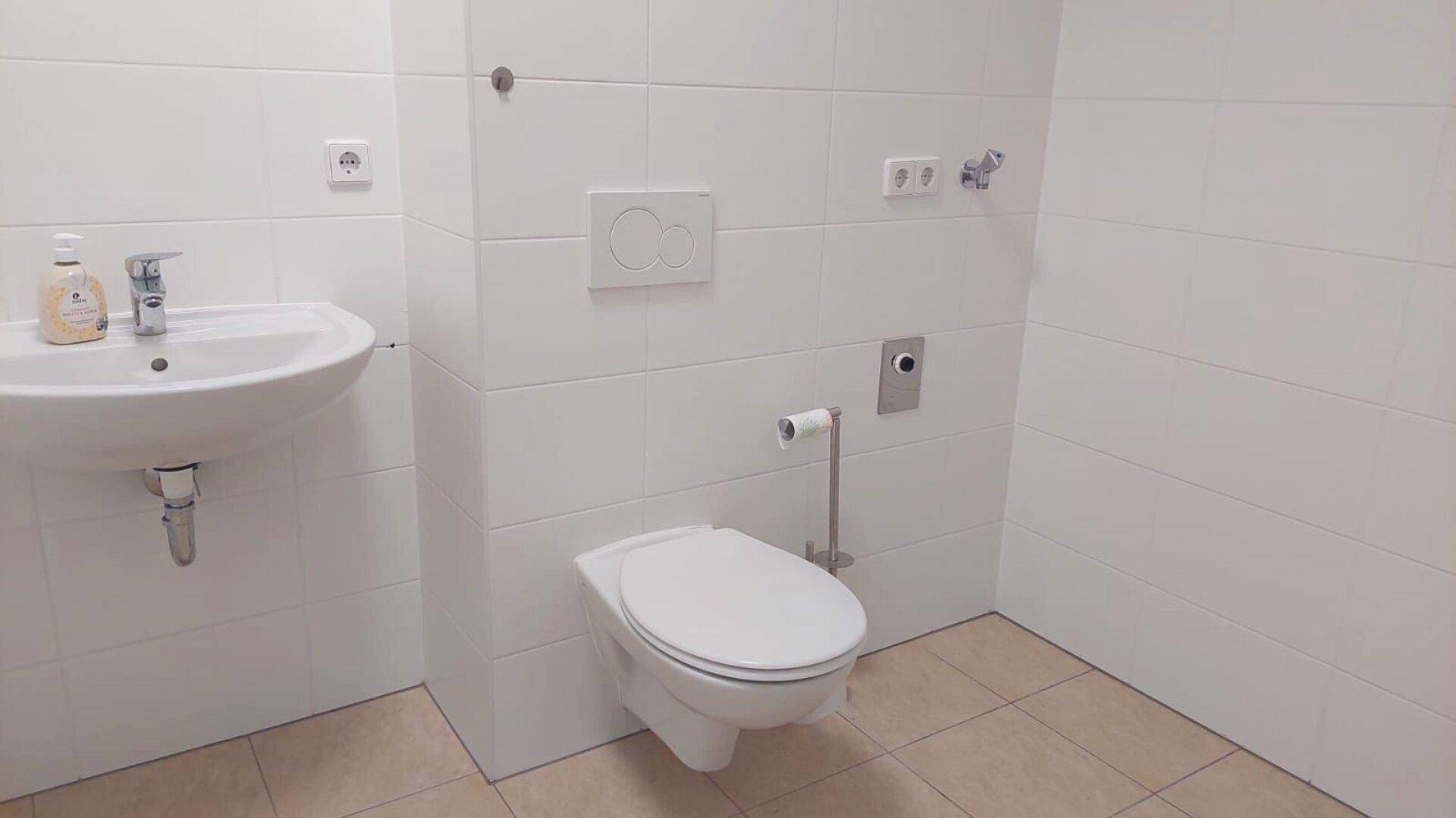 Modern gefliestes Badezimmer mit Waschbecken und wandhängender Toilette in hellem Design.