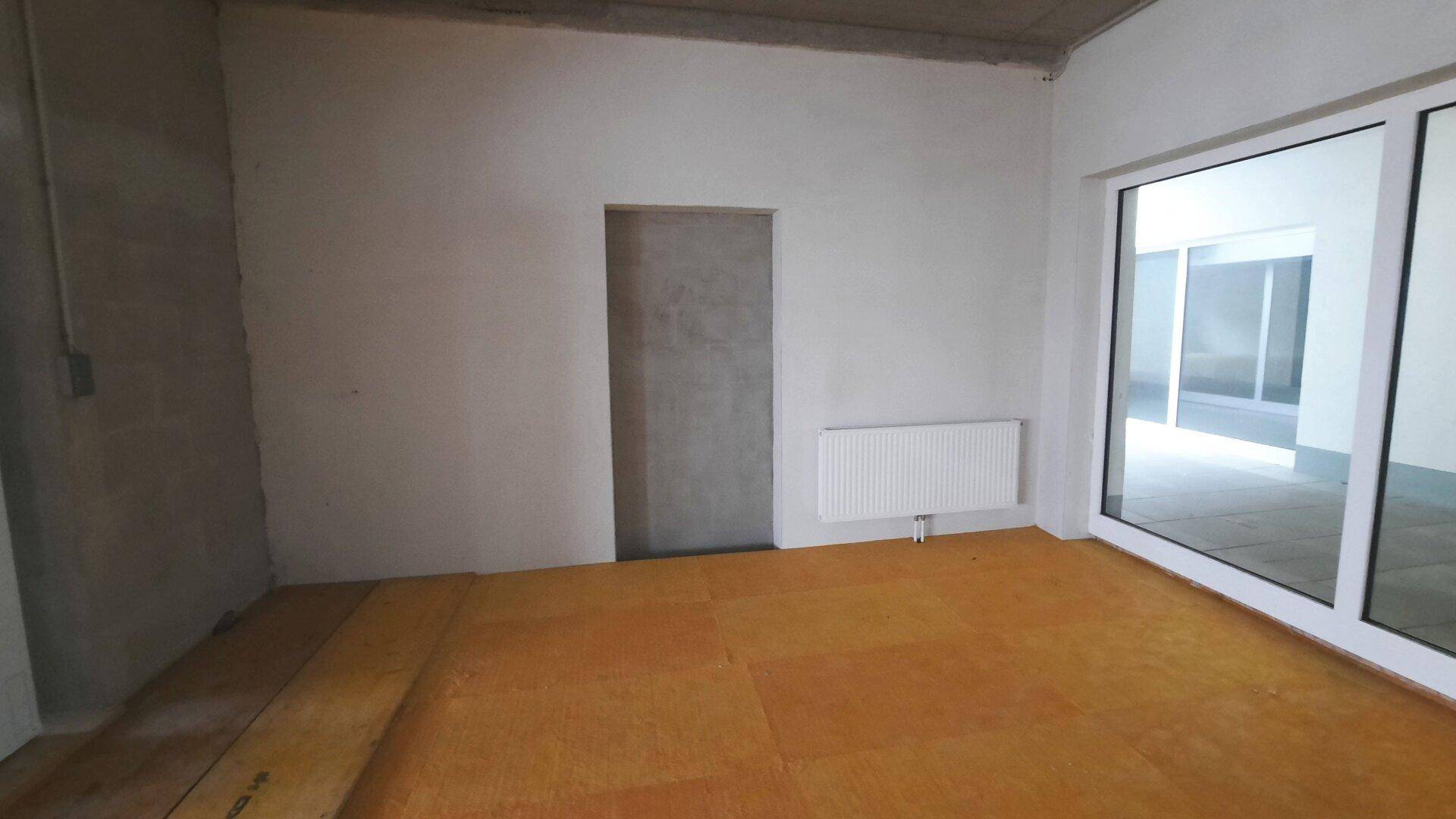 Ecke eines leeren Raumes mit Heizkörper, Türöffnung und großen Glasfronten.
