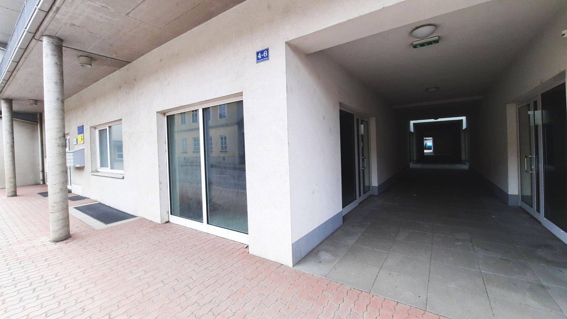 Fassade eines Geschäftsgebäudes mit mehreren Eingängen und einem überdachten Gehweg.