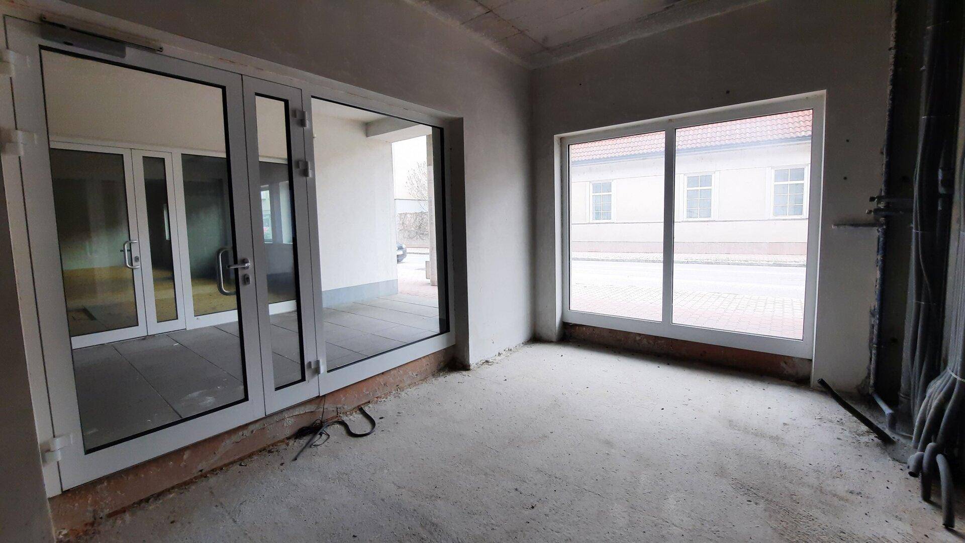 Unfertiger Gewerberaum mit großen Fenstern und Glastüren, bereit für den Ausbau.