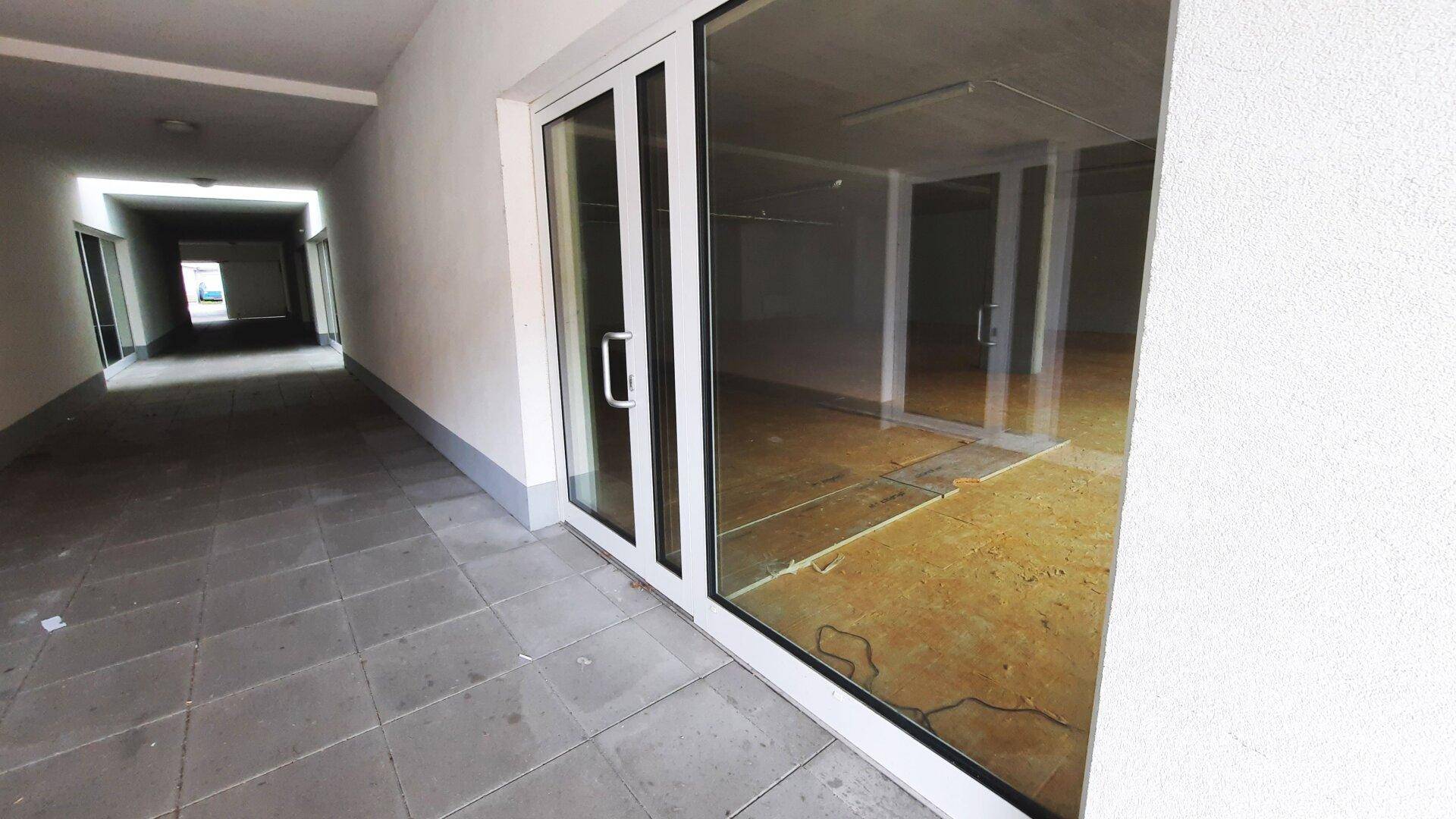 Eingangsbereich eines Gebäudes mit großen Glastüren und einem gefliesten Außenbereich.