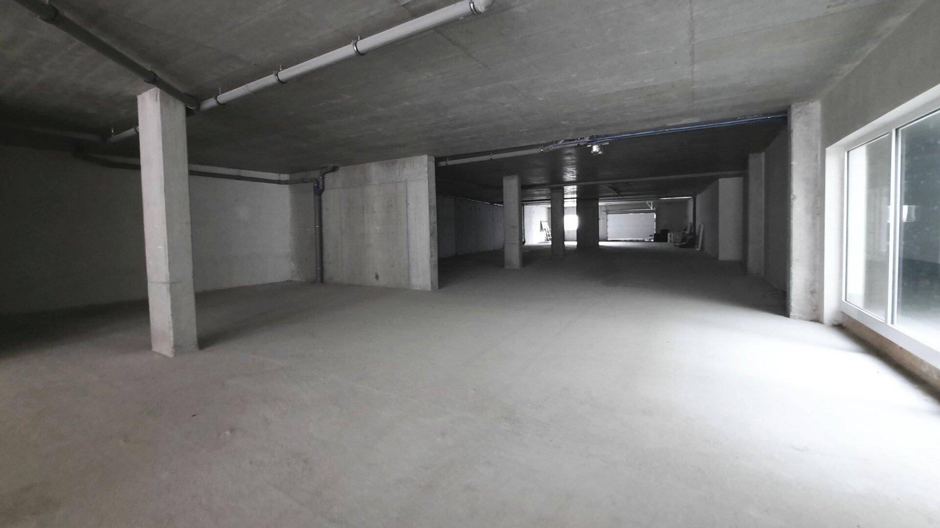 Großer, unfertiger Gewerberaum im Untergeschoss mit Betonsäulen und sichtbaren Leitungen.