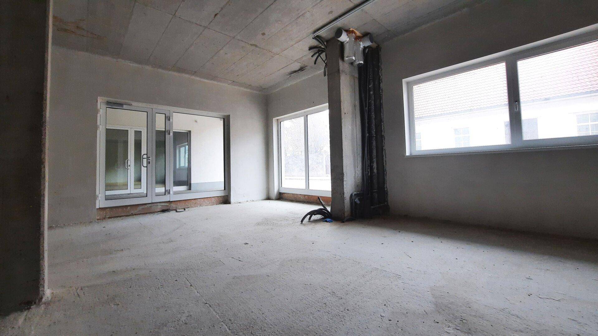 Unfertiger Gewerberaum mit großen Fenstern und einer Glastür, bereit für den Innenausbau.