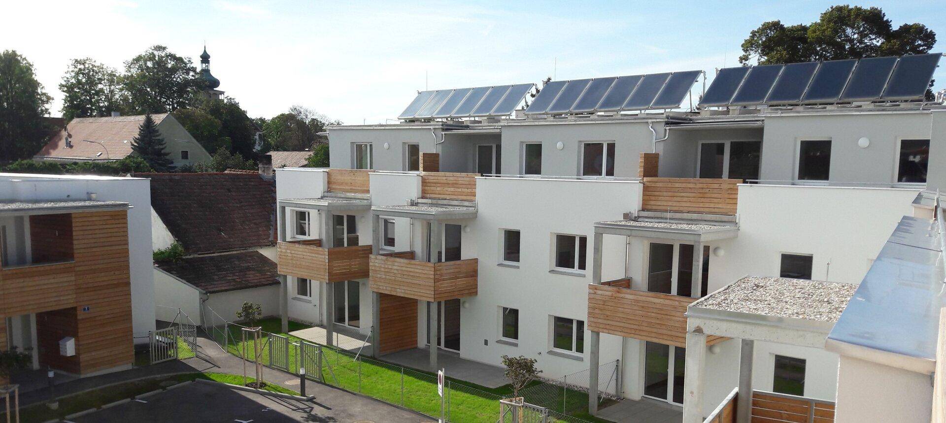 Moderne Reihenhäuser mit Balkonen, Photovoltaik-Systemen auf den Flachdächern und grüner Umgebung.