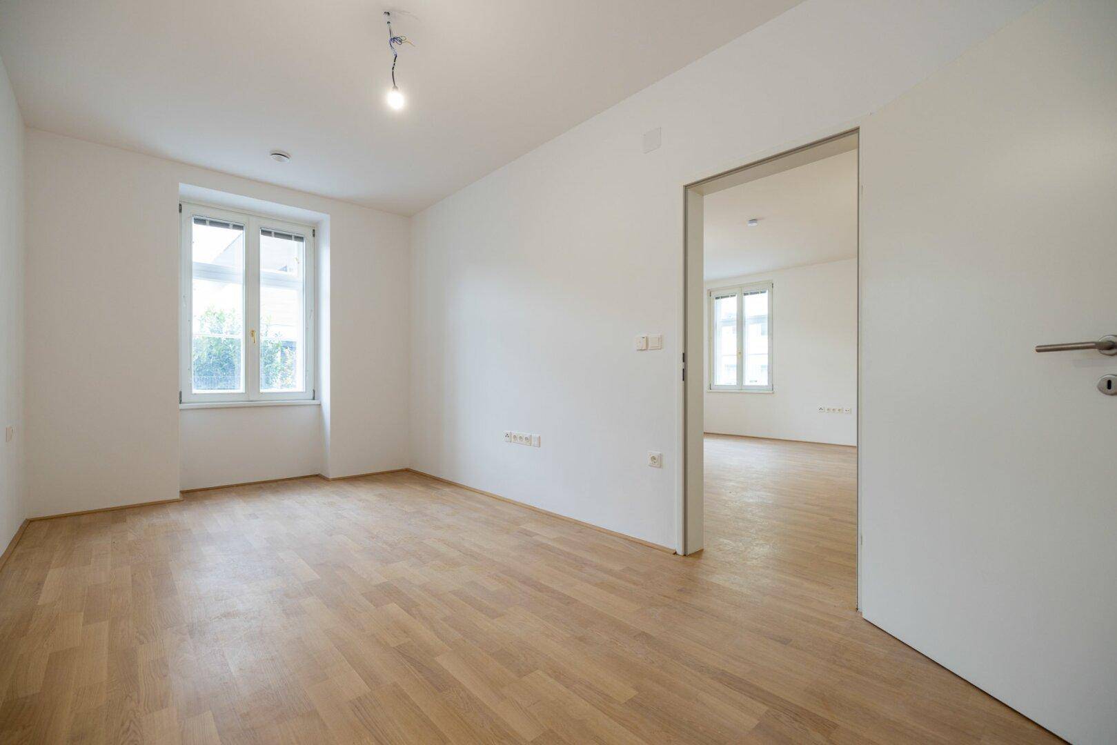 Heller Raum mit Parkettboden und einem Fenster, bereit zur Einrichtung als Schlaf- oder Arbeitszimmer.