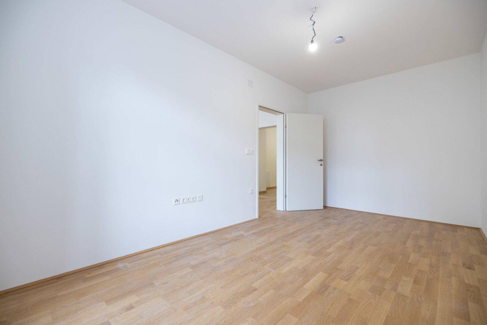 Geräumiger, heller Raum mit Parkettboden und Zugang zu einem weiteren Zimmer, vielseitig nutzbar.