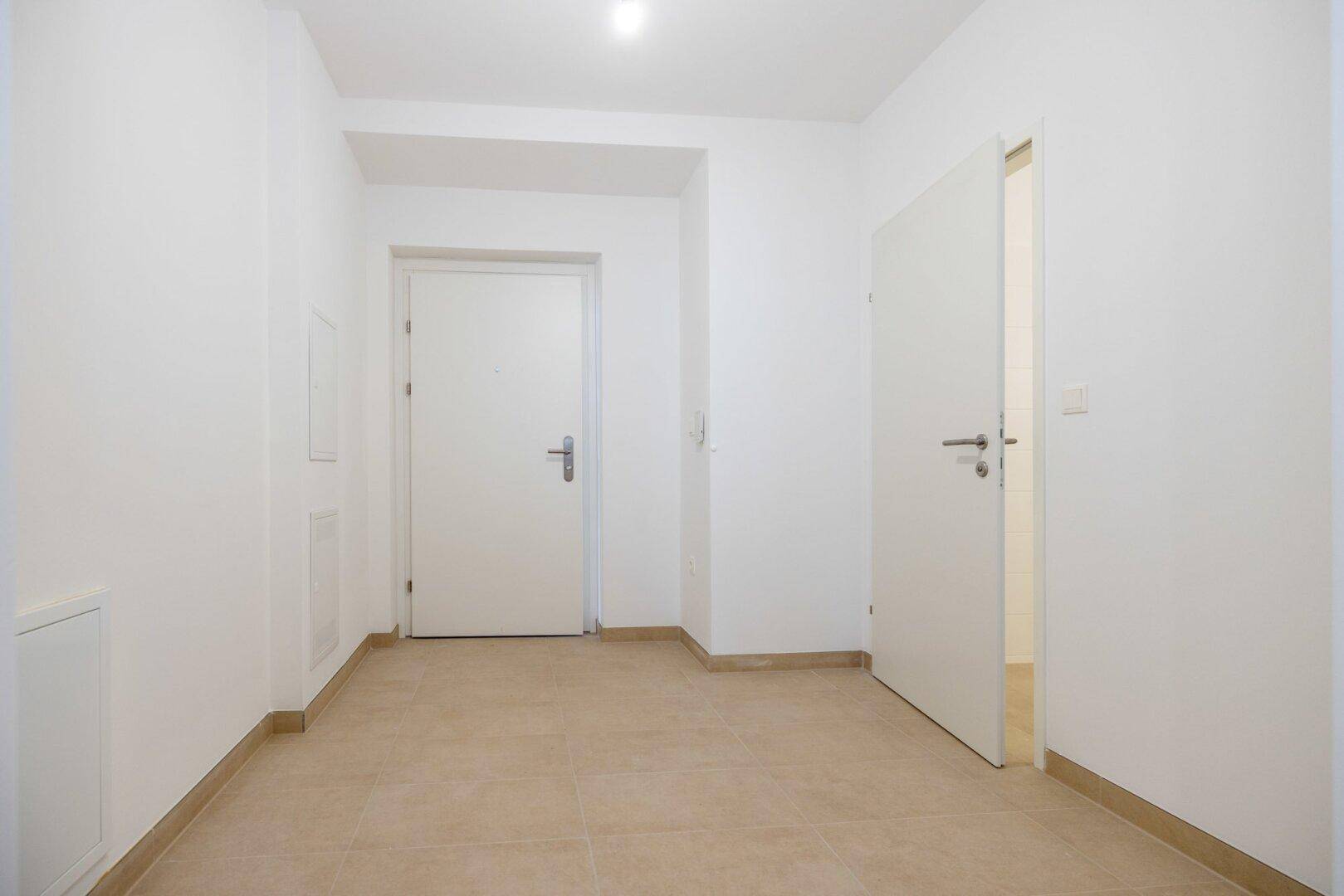 Heller Flur mit Fliesenboden und mehreren Türen, die zu verschiedenen Räumen führen.