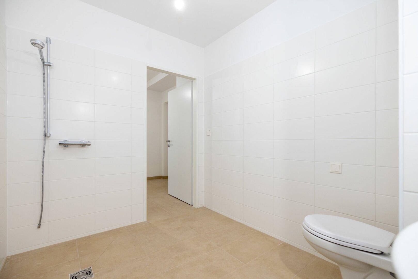 Modernes Badezimmer mit weiß gefliesten Wänden, ebenerdiger Dusche und Wand-WC.
