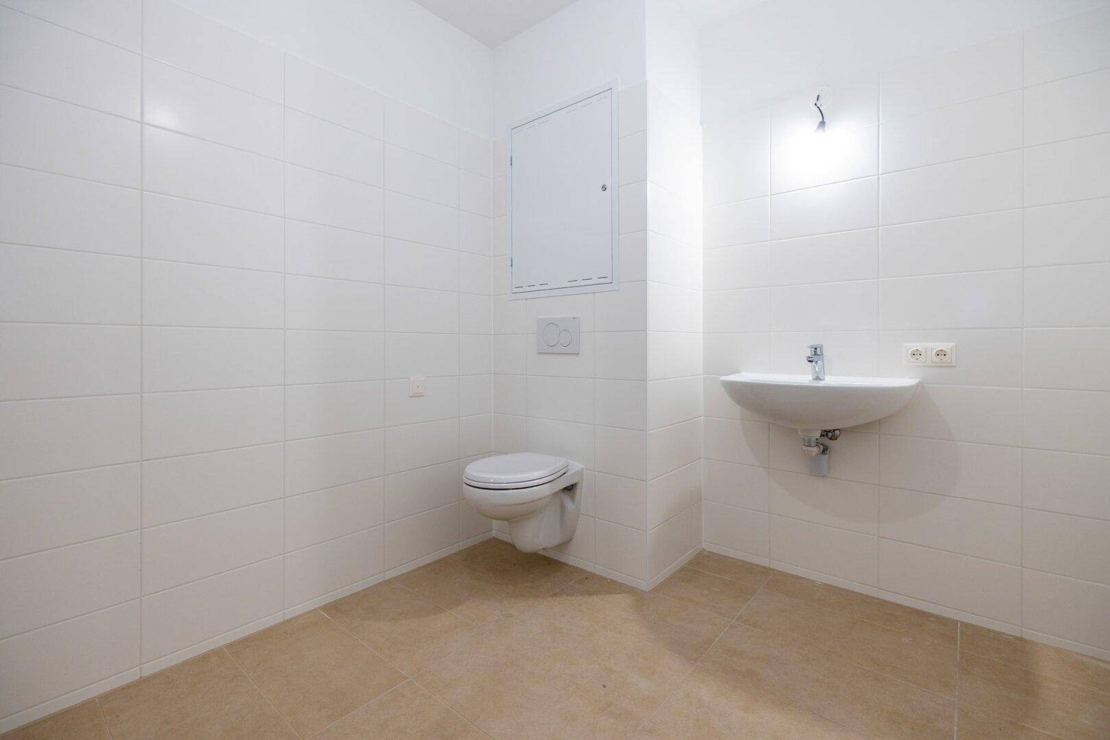 Helles Gäste-WC mit Wand-WC, Einzelwaschbecken und weißen Fliesen, funktional und sauber.